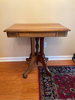 Full front view of vintage hall table showing rectangular top, central drawer, carved details on apron, turned central pedestal, and four legs ending in casters with one missing caster.