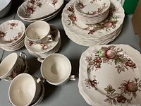 Full set of Johnson Brothers Harvest Time china showing plates, saucers, tea cups and serving bowls with the fruit and leaf pattern.