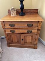 Front view of wooden nightstand showing two drawers with ornate metal handles over double doors with lock, placed on carpet.