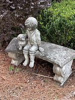 Stone bench featuring a young child sitting with a dog, placed outdoors on pine straw in front of bushes.