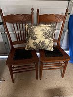 Pair of wooden side chairs with carved backs and toile pillow placed on one chair, showing front view and details.