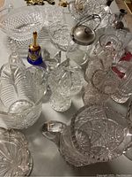 Assortment of clear pressed glass items showing vases, bowls, an ice bucket with silver lid, napkin rings, and a silver-plated candlestick on a table.