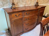 Front view of hardwood sideboard buffet showing six drawers and two cabinet doors with metal handles, curved design, polished medium-brown wood finish.