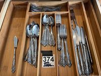 Full view of the flatware set organized in a wooden drawer, showing knives, forks, spoons, and teaspoons with ornate handles.