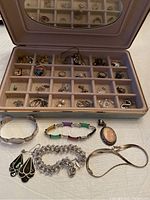 Open jewelry box showing rings, charms, pendants in compartments and laid out pieces in front