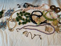 Wide shot of assorted vintage jewelry laid on a white cloth background including necklaces, earrings, a ring, and a watch.