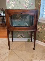 Front view of the antique vitrine table showing the glass front panel and wooden drawer with knob.