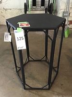 Full image of the black metal side table showing the hexagonal top and open-frame design, with a lot label indicating measurements 22 x 15 inches.
