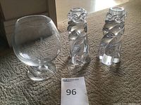 Two Baccarat crystal candle holders and one Baccarat crystal brandy snifter glass on carpet, with lot number card 96.