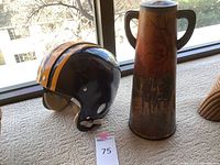 Photo of Bears black and yellow football helmet next to tall decorative metal urn on carpet by window.