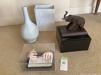 Wide shot of entire lot showing two vases, carved elephant on black base, and architect's hands sculpture in acrylic case