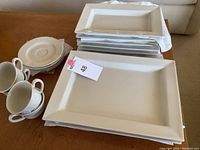 Set of stacked rectangular serving plates with crackle glaze next to stacked small round side plates and teacups with handles.