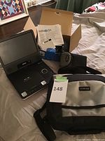 Philips portable DVD player open with screen, keypad, and remote control visible, Minolta camera box and carrying bag nearby