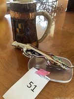 Photo showing a chrome Jaguar hood ornament mounted on a clear base next to a decorative stein mug with wooden and metallic detail on a wooden table.