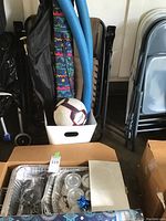 View of pool noodles, zero gravity chair, soccer ball, folding chairs and aluminum trays packed in a box.