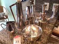 Group of six metal items on countertop: two vases, two pitchers, one bowl, one candlestick