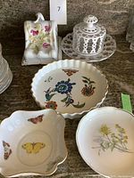 Overall view of porcelain serving pieces: two cheese plates with butterfly and floral motifs, white Royal Worcester tart pan, and a floral candy dish.
