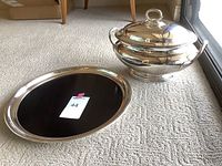 Photo showing full view of silver serving platter and covered serving bowl on carpet.