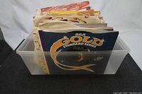 Plastic bin containing 84 vinyl record singles with various sleeve designs, mostly vintage 60s-80s styles