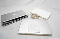 Three Apple laptops and power supplies arranged on surface with a handwritten note on top.