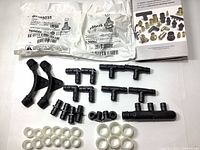 Photo showing a variety of black plastic plumbing fittings including tees, elbows, multi-port connectors, plugs, and multiple white rings arranged on a white background.