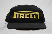 Front view of black baseball cap with large yellow Pirelli logo embroidered on front.
