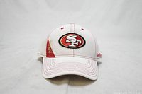 Front view of the white San Francisco 49ers baseball-style cap showing the embroidered logo patch and red stitching details.