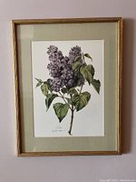 Full view of framed lilac botanical print hanging on wall, showing gold-tone textured frame and beige mat.