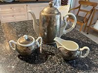 Overall view of the three-piece tea set including teapot, sugar bowl, and creamer on a granite countertop.