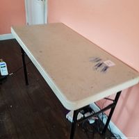Full view of the 4ft plastic table showing beige top and black metal legs, with visible scratches and paint marks on surface
