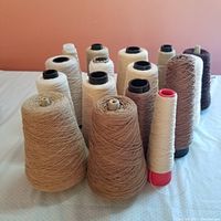 Photo showing several cones of cotton thread in assorted neutral colors such as beige, cream, tan, and dark brown.