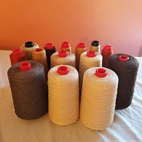Overview of multiple cones of cotton thread in assorted colors on an off-white surface against a peach background.