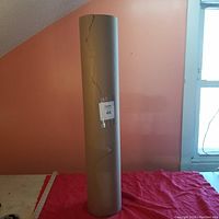 Full view of the brown kraft paper roll standing upright, showing its height and overall cylindrical shape with visible cracks and tears.