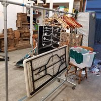 Full view of the metal clothing rack with hangers and a folded table leaning against it.