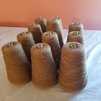 Overview of eleven cones of soft antelope brown cotton thread on a surface.
