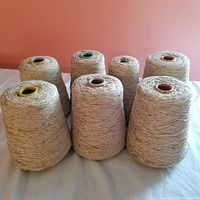 Seven cones of bisque brown rayon chenille yarn arranged on a flat surface showing overall quantity and color.