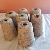Seven cones of luxury fawn brown rayon chenille yarn upright on a table.