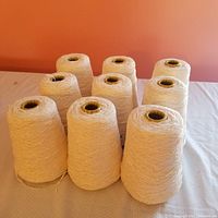 Nine cones of ivory white rayon chenille yarn arranged on a surface, showing texture and volume.
