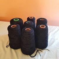 Eight cones of dark midnight blue rayon chenille yarn arranged together, showing full cones with different colored inner cone centers.