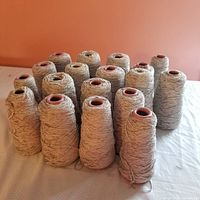 Seventeen cones of rayon chenille yarn in a muted nickel gray color arranged in a group on a table showing the full lot quantity and overall condition.