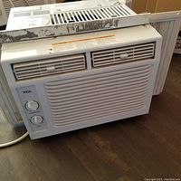 Front view of the TCL window air conditioner showing the vented panel, brand logo, and two manual control dials for temperature and mode settings.