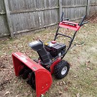 Side view of the red Yard Machines snowblower with engine and discharge chute visible