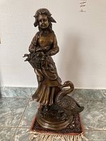 Front view of bronze sculpture showing woman holding basket and goose at base