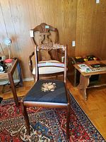 Two wood frame chairs positioned near a wooden wall and on a patterned rug, showing needlepoint and upholstered seats