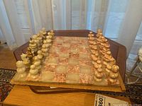 Top-down view of heavy stone chessboard set with carved stone chess pieces in light and reddish tones, arranged for gameplay.