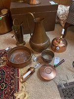 Full view of all copper and brass vessels grouped together on carpet showing their variety and condition.