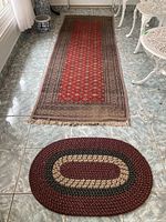 Kilim carpet with fringe edges and small oval woven mat placed in front, showing overall colors, pattern and condition of both items.