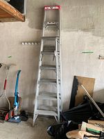 Front view of 8-foot aluminum step ladder standing upright against wall with some clutter.
