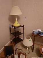 Two table lamps shown, one on a small wooden shelving unit and the other on the floor. Various picture frames and dishes visible nearby.