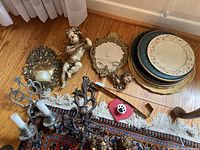 Overview of lot showing mirrors, figurines, plates, pairs of metal sconces and ladle laid on floor
